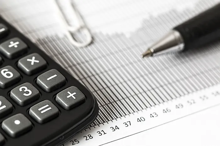 Calculator and pen on a bar graph, representing finance and payroll