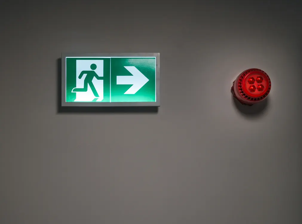 Illuminated emergency exit sign in a corridor, indicating a fire escape route